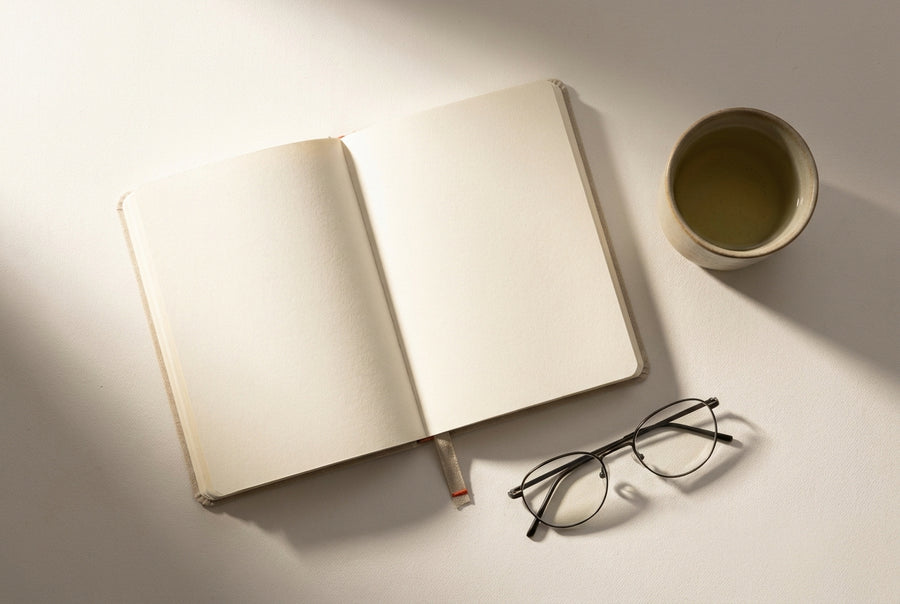 Minimal desk with open notebook and green tea in soft morning light, seen from above
