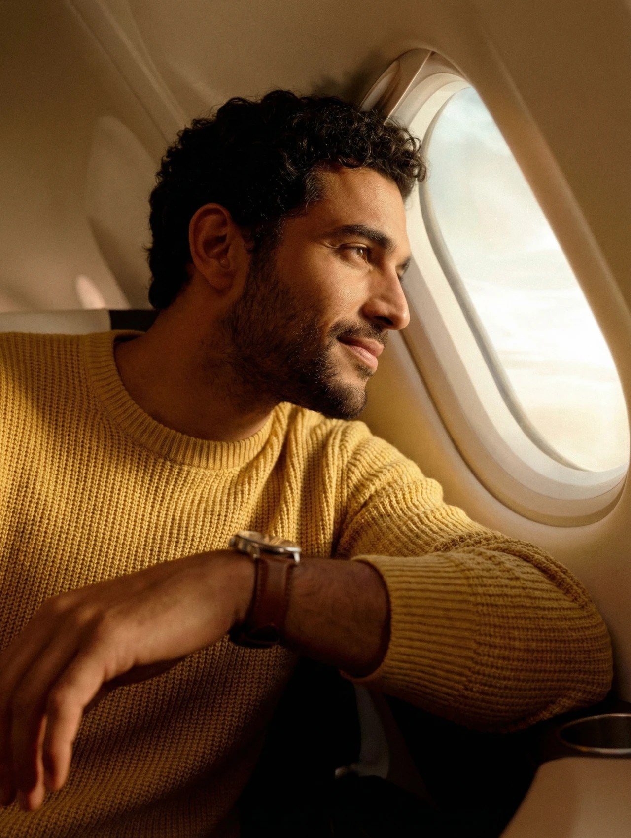 Man in a yellow knit looking out of an aircraft window at golden hour