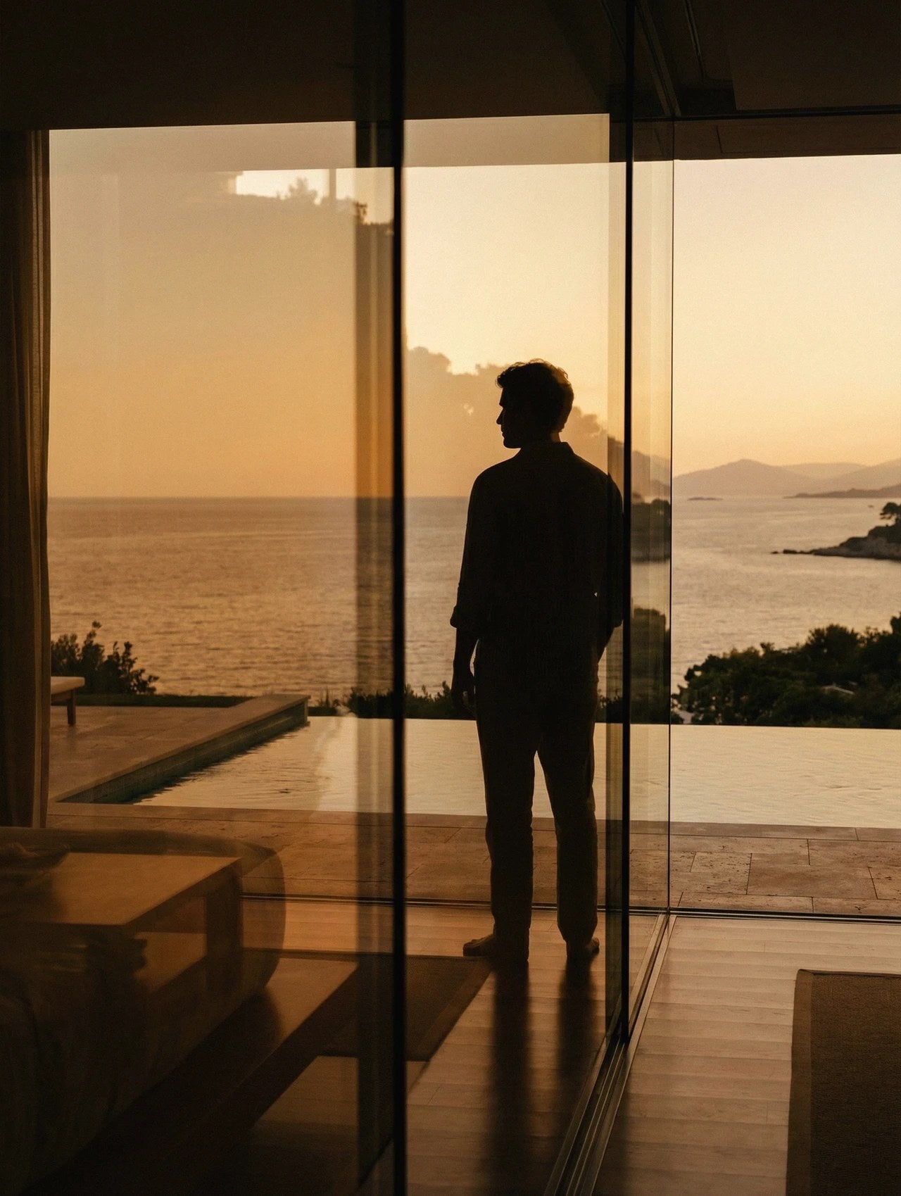 Silhouette at a glass wall, looking out over the sea at sunset